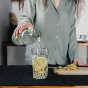 Woman pours water for lemon ginger infusion, promoting health and hydration.